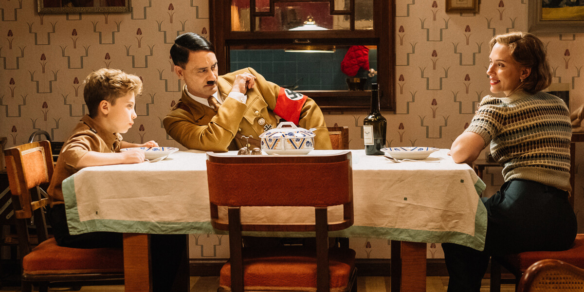 A still from the film, Jojo Rabbit. (Left to right): Jojo (Roman Griffin Davis) has dinner with his imaginary friend Adolf (Writer/Director Taika Waititi), and his mother, Rosie (Scarlet Johansson). Photo by Kimberley French. © 2018 Twentieth Century Fox Film Corporation All Rights Reserved