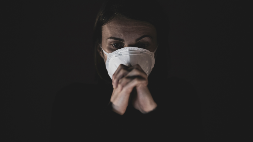 woman in mask sits in the dark with a worried look on her face. mental health