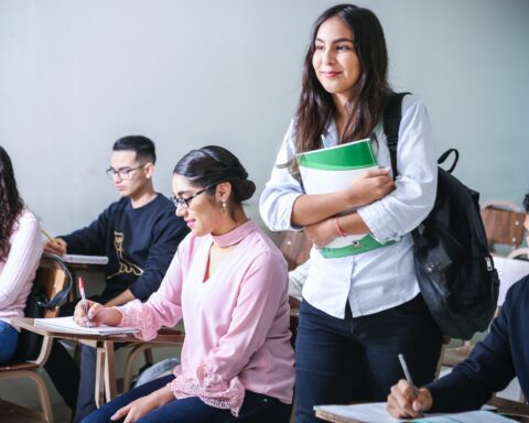 A joung woman carrying a textbook in a classroom.