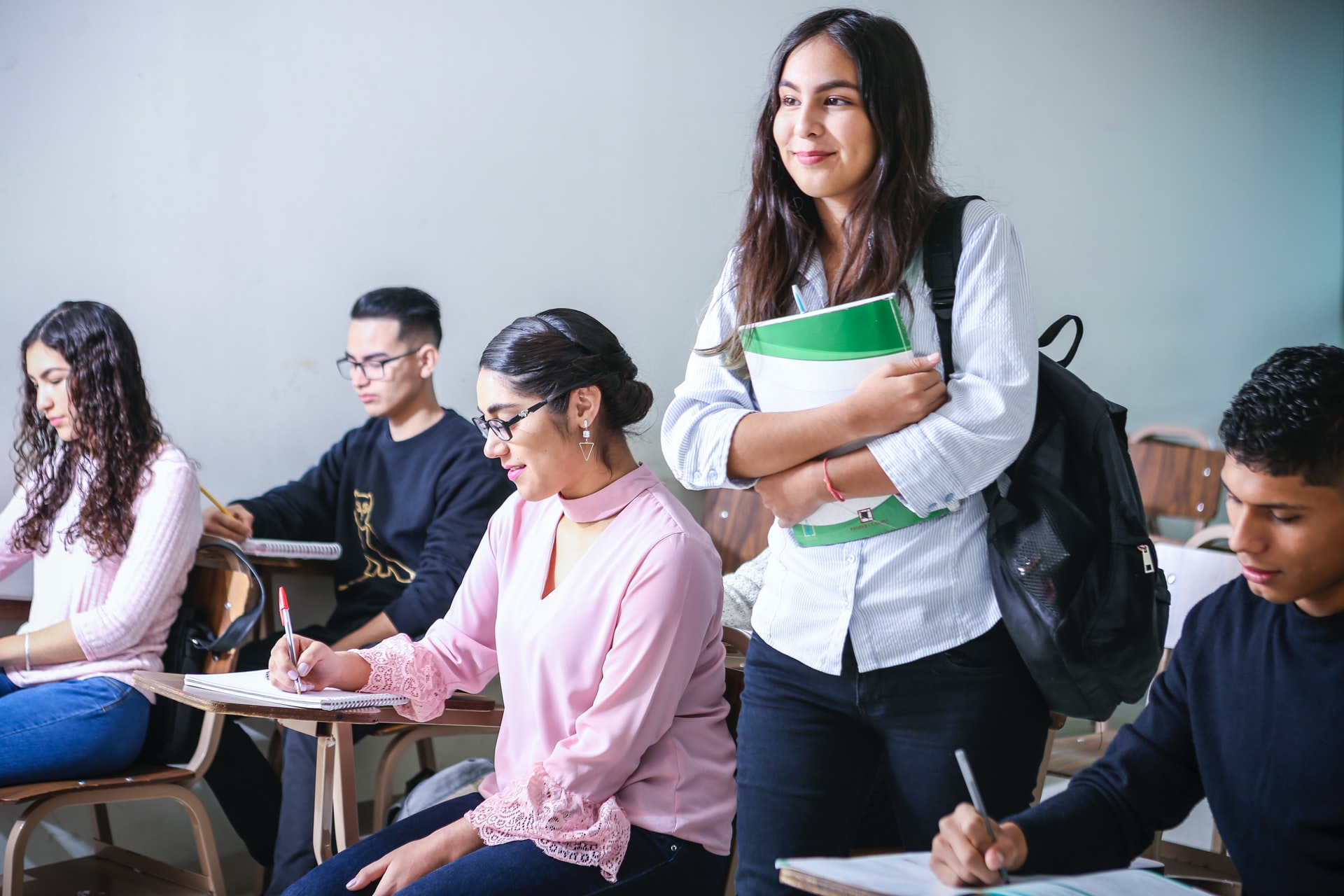 A joung woman carrying a textbook in a classroom.