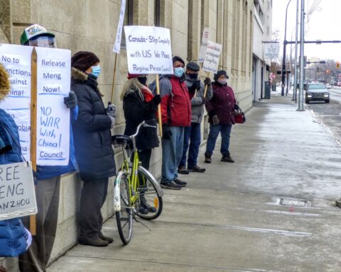 Seven people in winter clothing and face masks line the street in Regina, holding placards that read: "Free Meng Wanzhou," "No sanctions against China," "No war with China."