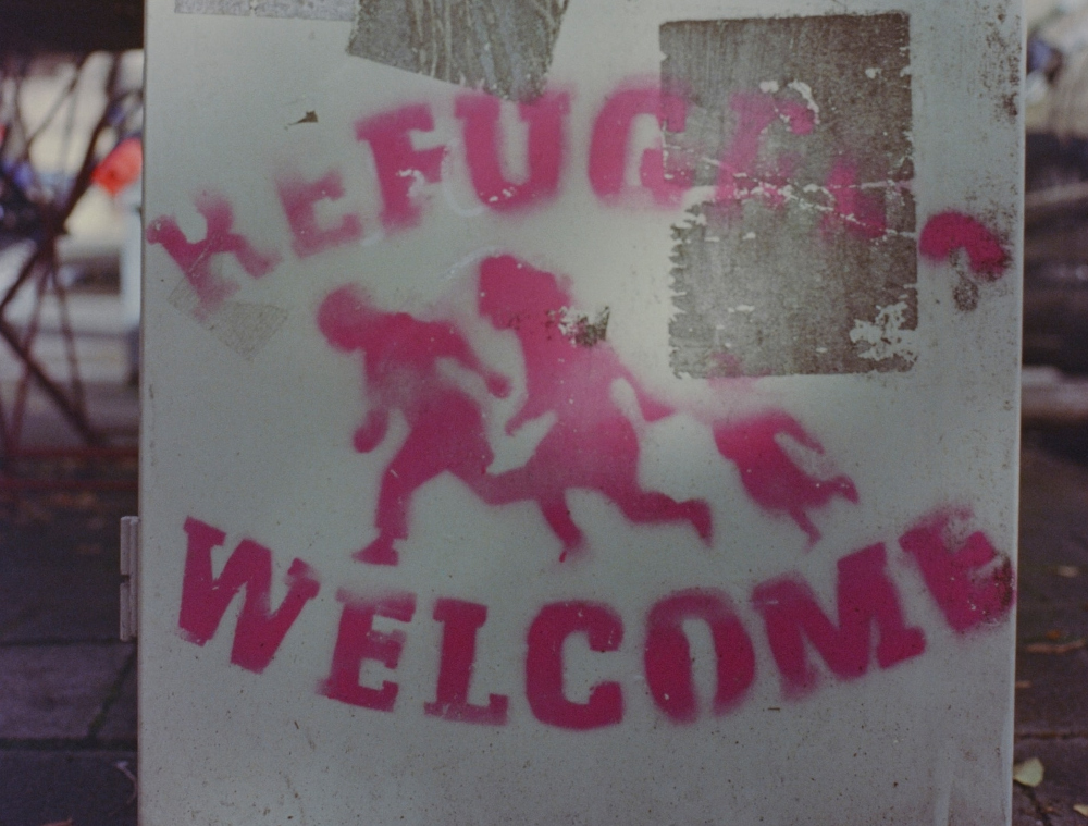 PhPhoto of a sign that reads "Refugees Welcome" and a graphic representation of people running.