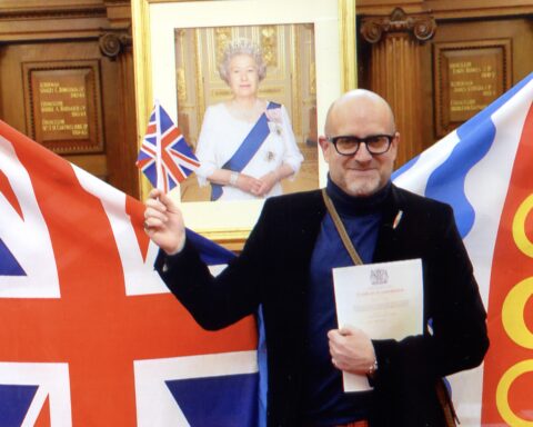 Canadian artist, Owen Grant Innes pictured at dual citizenship ceremony with Queen Elizabeth II's framed picture in the background