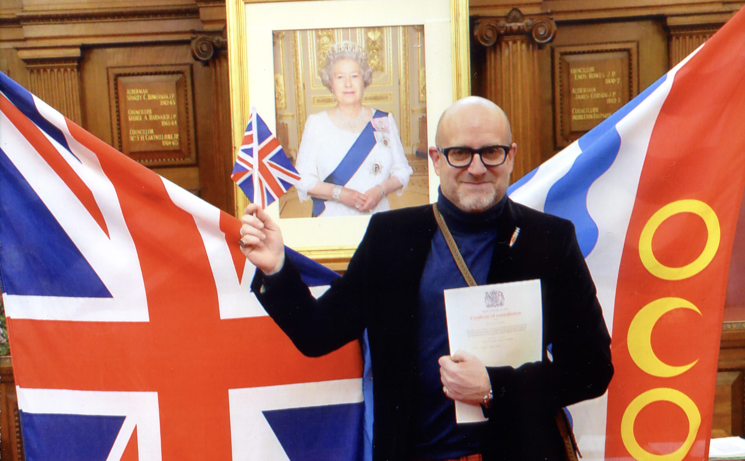 Canadian artist, Owen Grant Innes pictured at dual citizenship ceremony with Queen Elizabeth II's framed picture in the background