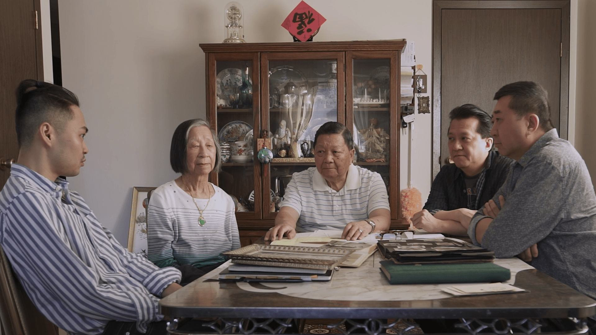 The Chow family and director Weiye Su seated around a dining table covered in photo albums.